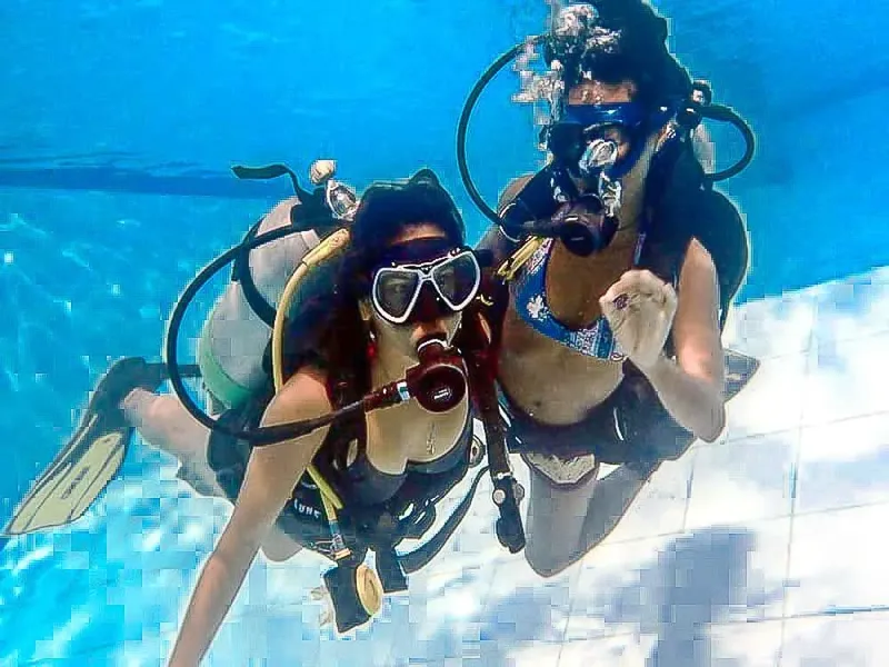 Deux plongeuses souriantes en piscine, équipées de masques et de bouteilles