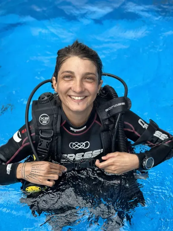 Plongeuse souriante avec son équipement complet dans une eau turquoise