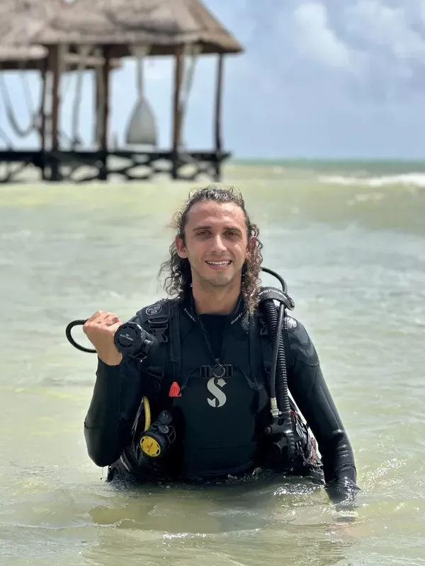 Plongeur souriant en combinaison, équipé, dans l'eau peu profonde