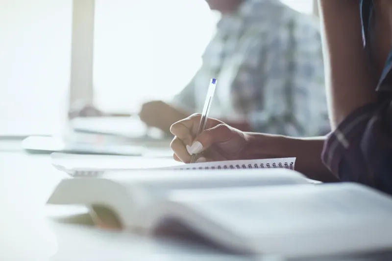 Personne prenant des notes en classe, lumière naturelle, ambiance studieuse