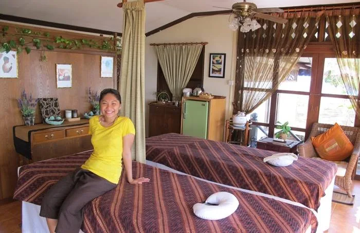 Femme souriante assise sur des tables de massage dans une pièce décorée