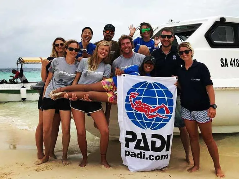 Groupe de personnes souriantes posant avec un drapeau PADI sur une plage