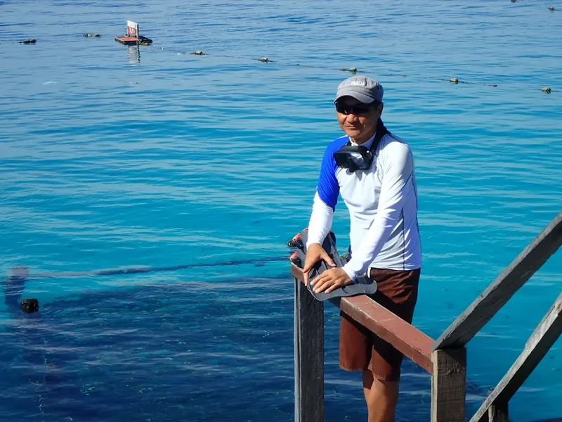 Plongeur sur un ponton, tenant masque et palmes, mer turquoise