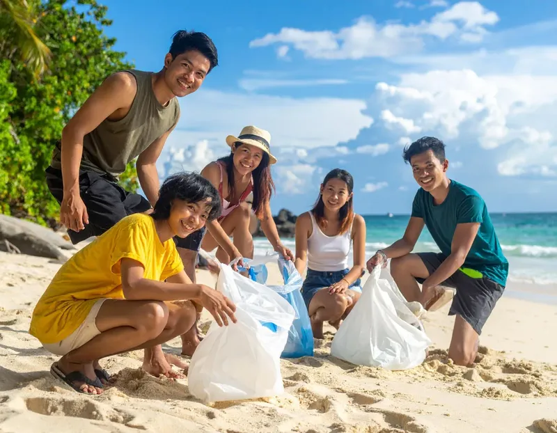 Groupe de jeunes souriants ramassant des déchets sur une plage ensoleillée