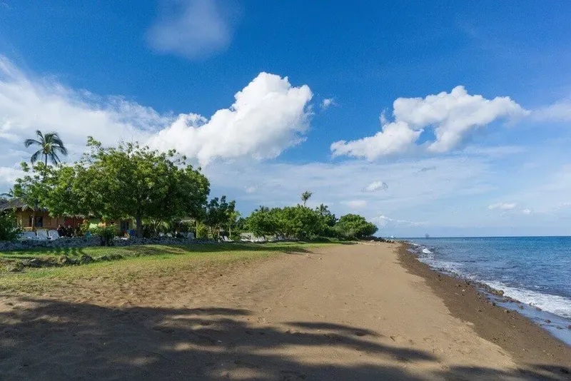 Plage de sable, végétation tropicale, bâtiments et ciel bleu nuageux
