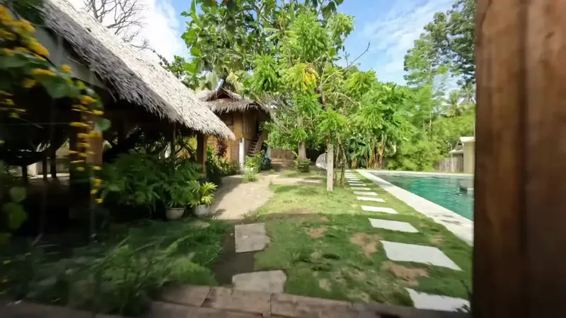 Petits bâtiments avec toits de chaume, piscine et végétation tropicale