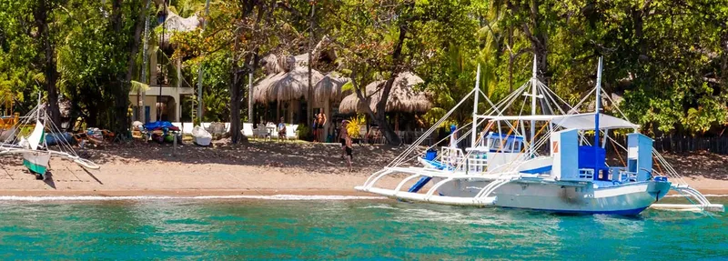 Bateau traditionnel amarré devant une plage et des huttes de chaume