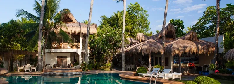 Bâtiments avec toits de chaume, piscine et végétation tropicale ensoleillée