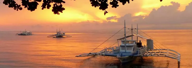 Trois bateaux de pêche au coucher du soleil sur une mer calme