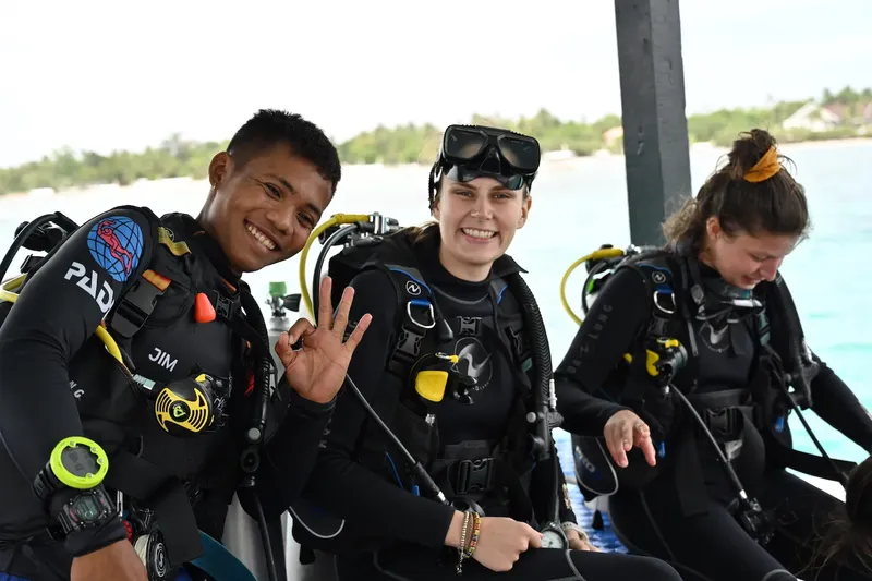 Trois plongeurs souriants équipés prêts pour une immersion en mer