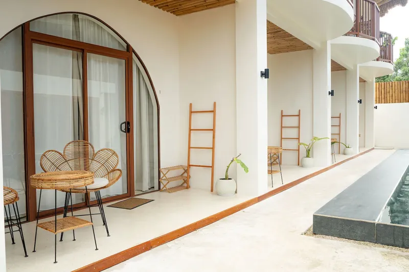 Terrasse avec mobilier en rotin devant des chambres blanches ouvertes