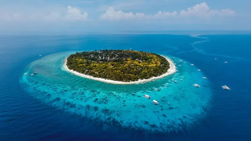 Île tropicale entourée d'eau turquoise et de bateaux de plaisance