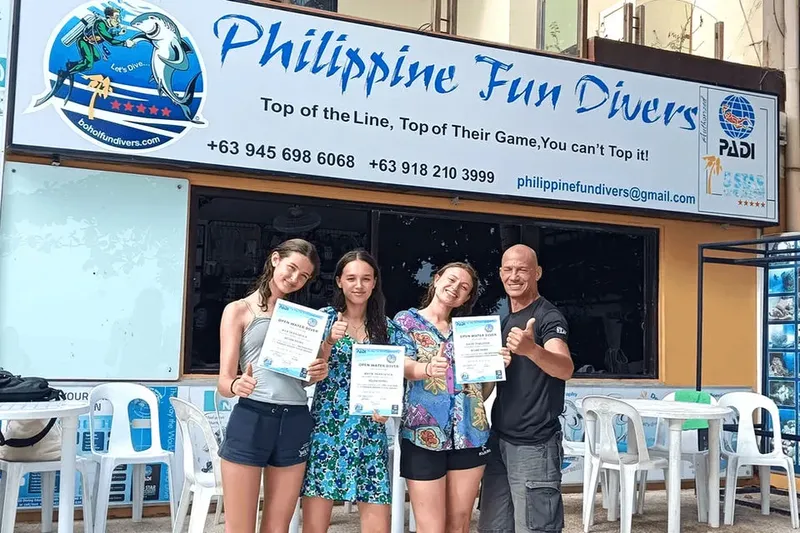 Quatre personnes souriantes présentent leurs certificats de plongée devant un centre