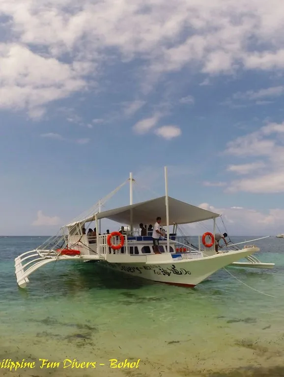 Bateau de plongée blanc avec des passagers, mer turquoise et ciel nuageux