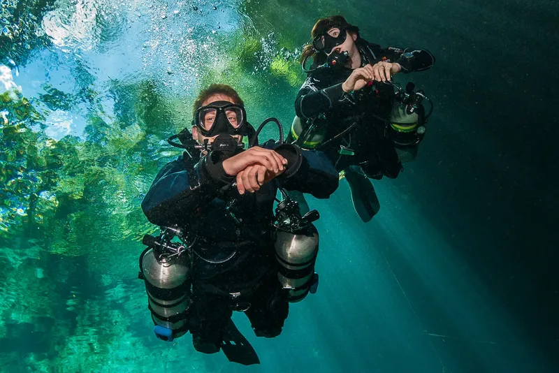 Deux plongeurs souriants avec leur équipement en milieu aquatique clair