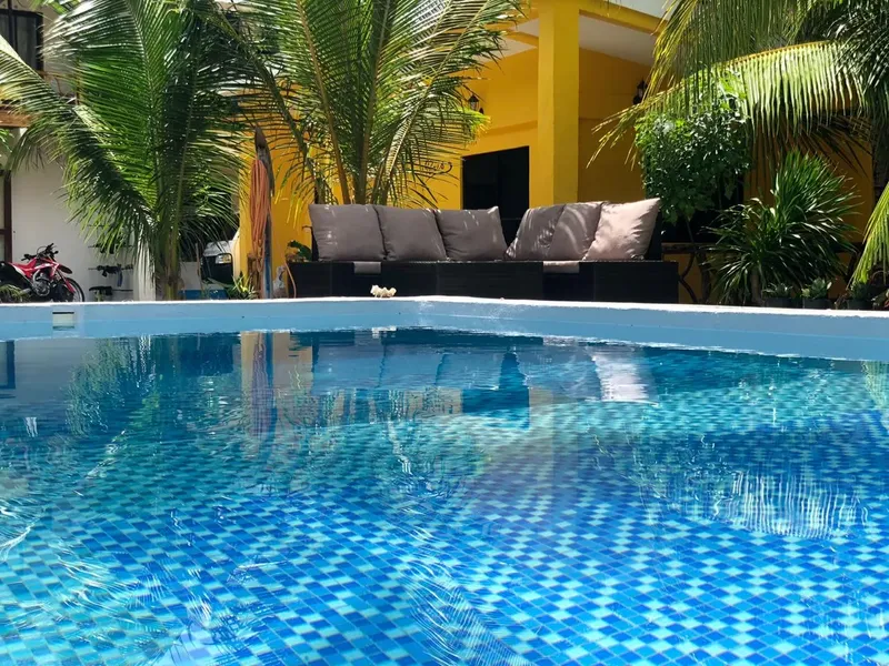 Piscine carree bleue avec un salon de jardin et palmiers