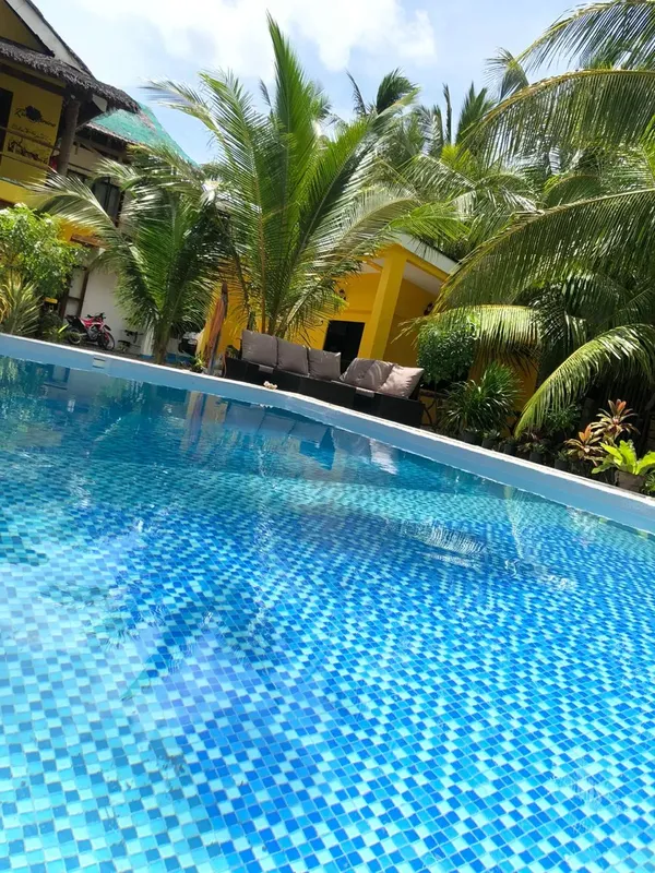 Piscine carrelée bleue avec végétation luxuriante et bâtiments colorés