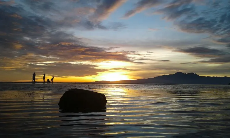 Trois silhouettes sur une plage au coucher du soleil, mer calme