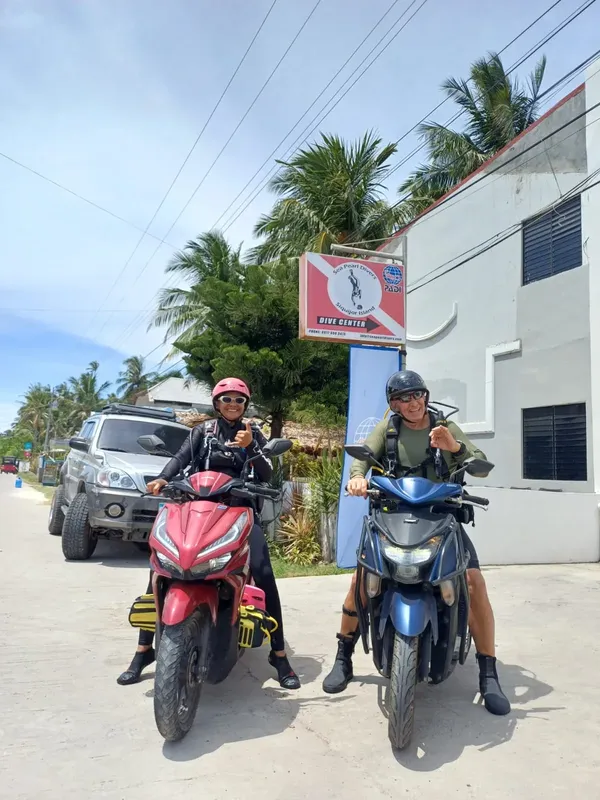 Deux plongeurs souriants sur des scooters devant un centre de plongée