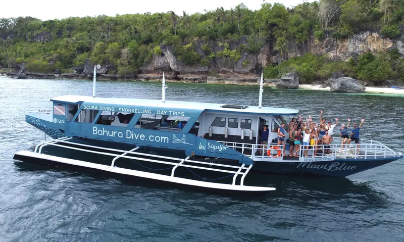 Bateau de plongée bleu avec des passagers souriants et levant les bras