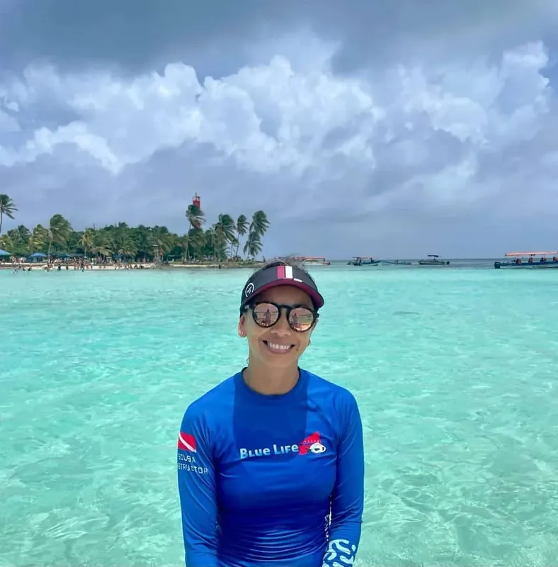 Femme souriante en tenue de plongée devant une mer turquoise et des palmiers