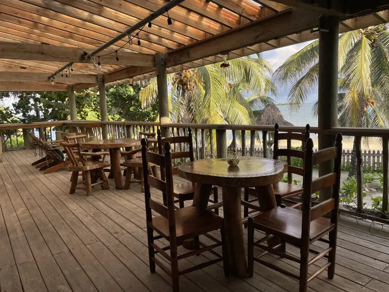 Terrasse en bois avec tables et chaises, vue sur mer et végétation