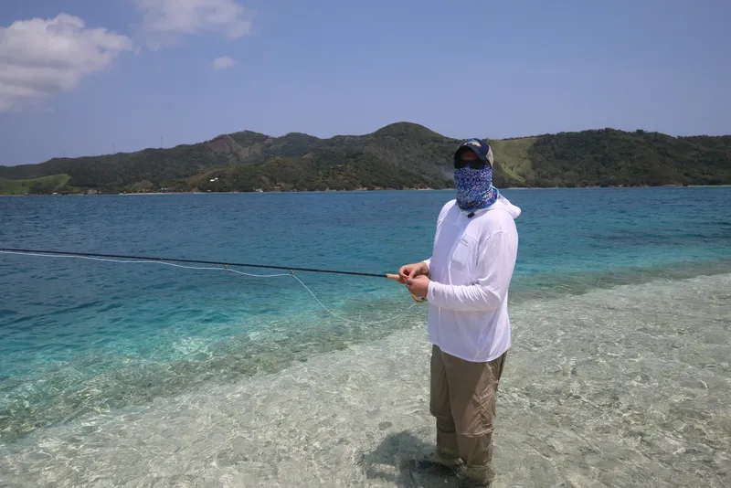 Homme pêchant dans une eau turquoise peu profonde avec un paysage montagneux