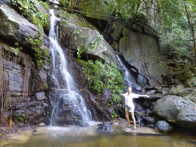 Une femme se tient devant une cascade dans une forêt tropicale