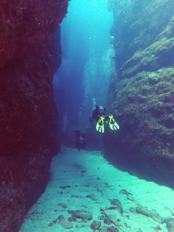 Plongeur explorant une fissure rocheuse sous-marine dans une eau claire