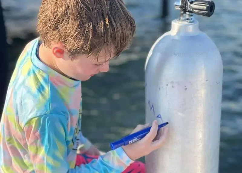 Un enfant écrit sur une bouteille de plongée avec un stylo