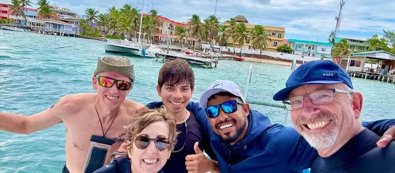 Quatre personnes souriantes sur un bateau en mer, paysage tropical