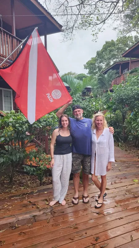 Trois personnes souriantes posent devant un drapeau PADI et un bâtiment