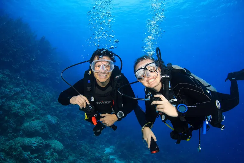 Deux plongeurs souriants, masque et combinaison, dans une eau bleue