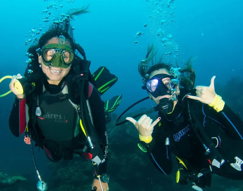 Deux plongeurs souriants font des signes de la main sous l'eau