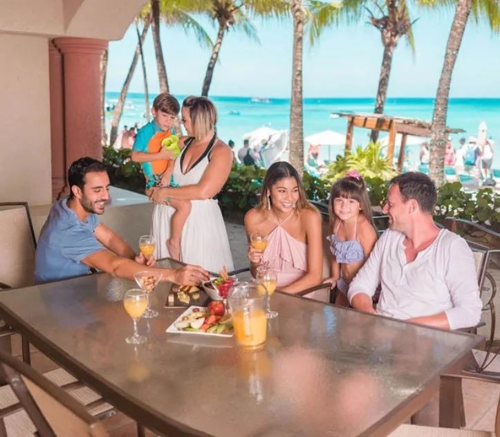 Famille souriante partageant un repas ensoleillé sur une terrasse tropicale
