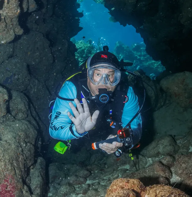 Plongeur en grotte sous-marine, main levée, regardant vers l'objectif