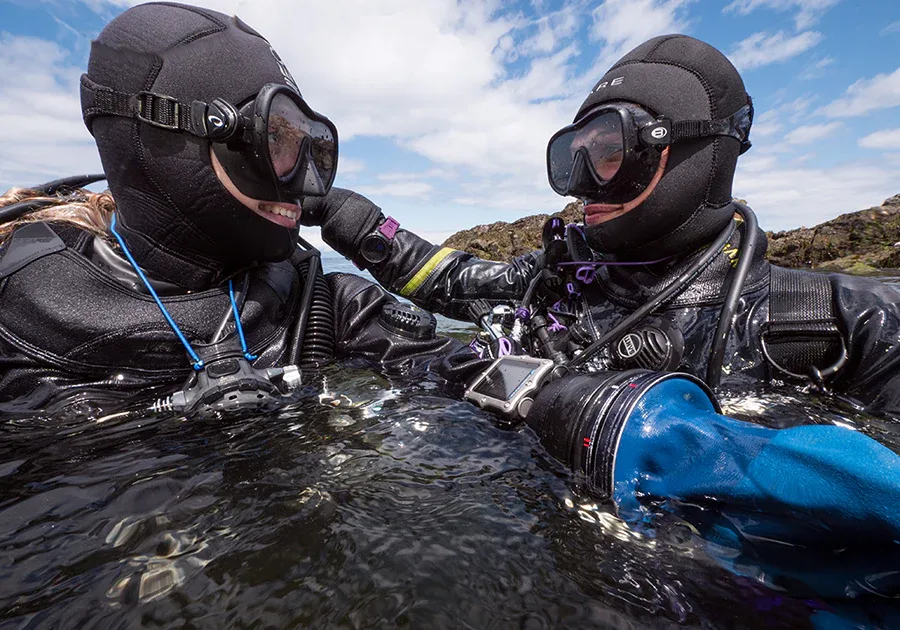 Deux plongeurs en combinaison étanche communiquent sous la surface de l'eau