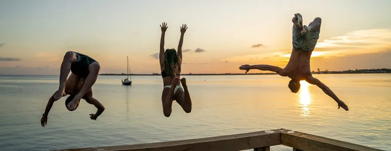 Trois personnes sautent d'un ponton au coucher du soleil en mer