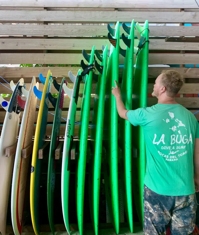 Homme rangeant des planches de surf vertes dans un support en bois
