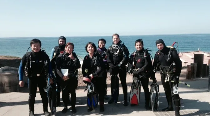 Groupe de plongeurs souriants équipés sur un quai ensoleillé