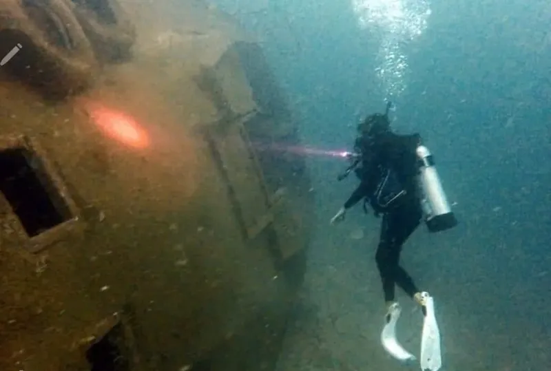 Plongeur explore une épave sombre avec des bulles et lumière
