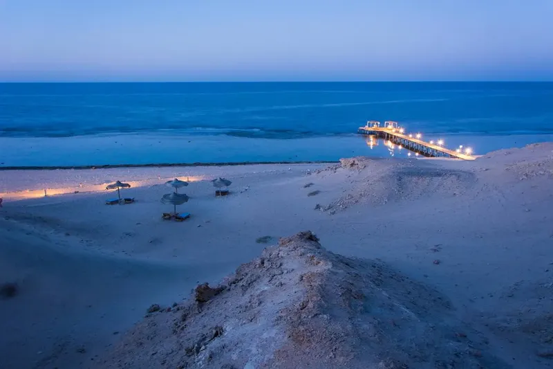 Plage de sable avec parasols et ponton illuminé au crépuscule
