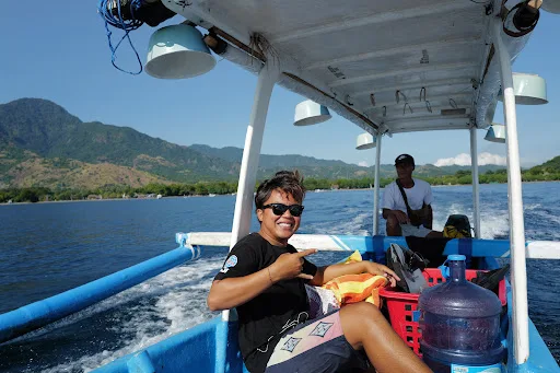 Deux personnes souriantes sur un bateau en mer, paysage montagneux