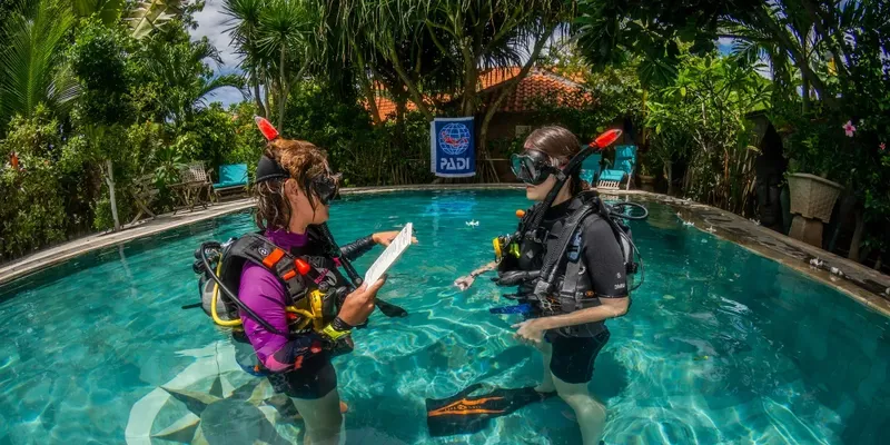 Deux plongeurs en formation discutent près d'une piscine avec logo PADI