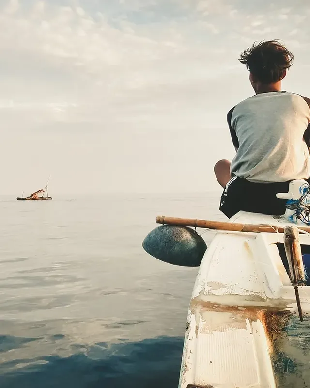 Homme assis sur un bateau regardant vers un autre bateau en mer