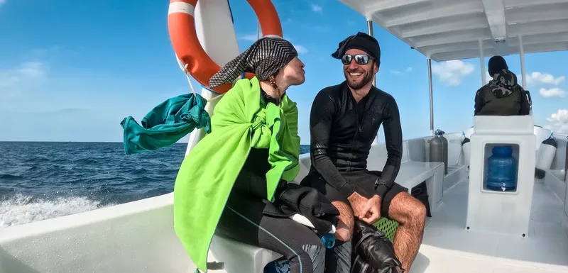 Deux plongeurs souriants sur un bateau en mer, équipés et détendus