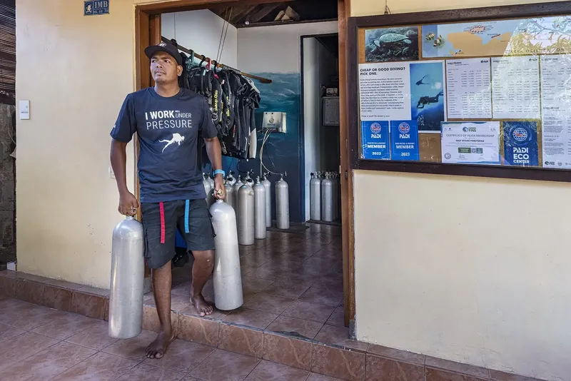Homme transportant des bouteilles de plongée devant un centre de plongée