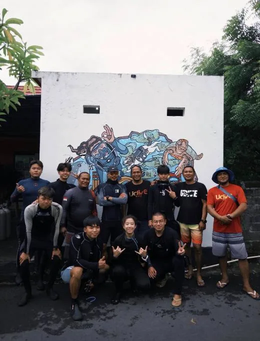 Groupe de plongeurs souriants posant devant une fresque marine colorée