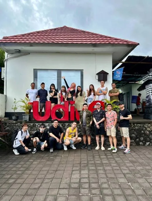 Groupe de personnes souriantes posant devant un bâtiment et un logo rouge