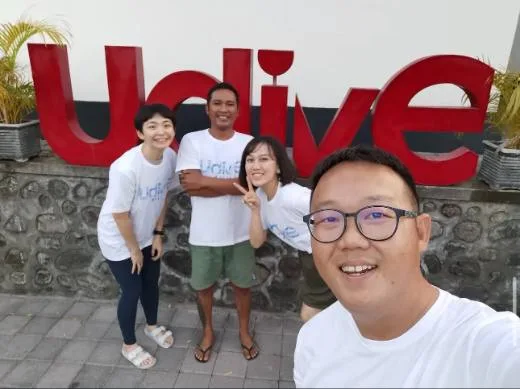 Quatre personnes souriantes posent devant une grande inscription rouge